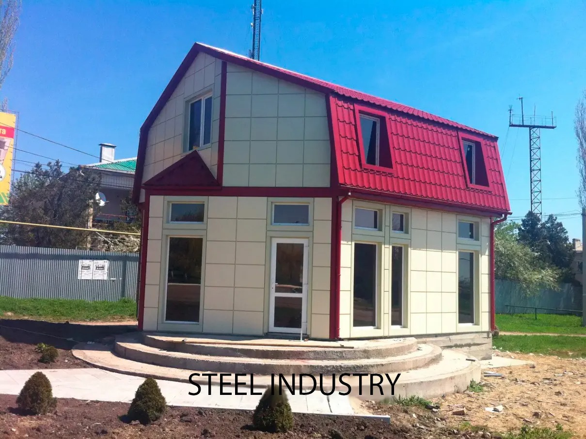 Niewielki budynek z elewacją z paneli w jasnym kolorze i czerwonym dachem z blachy trapezowej, widoczny z zewnątrz w słoneczny dzień.