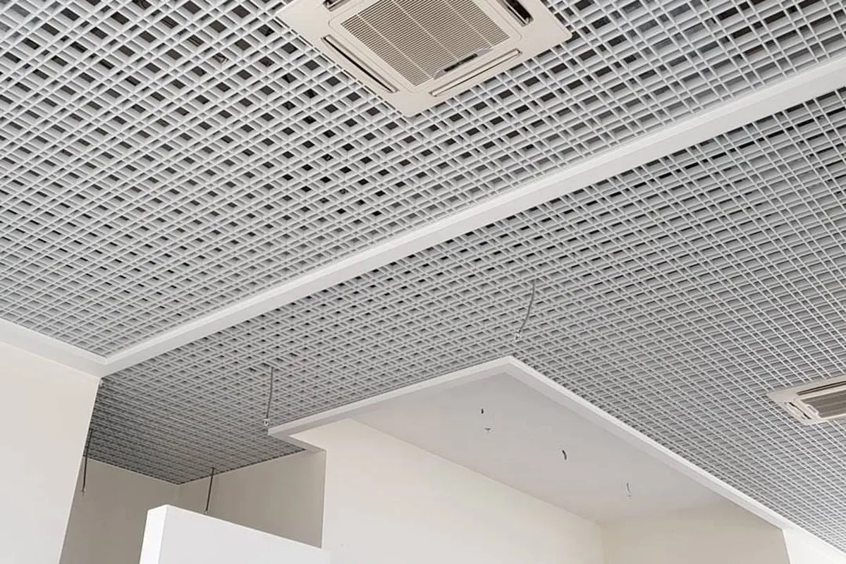 Biały sufit podwieszany z kratką i wbudowanymi klimatyzatorami, widoczne elementy mocujące.
