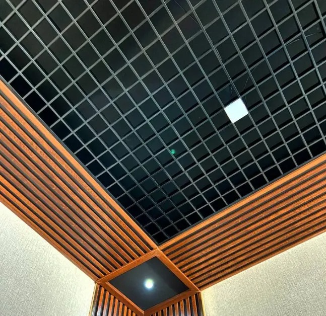 Czarny sufit kasetonowy z podwieszaną konstrukcją w kształcie kratownicy, otoczony dekoracyjnymi panelami z drewnopodobnych listew, oświetlony punktowo.