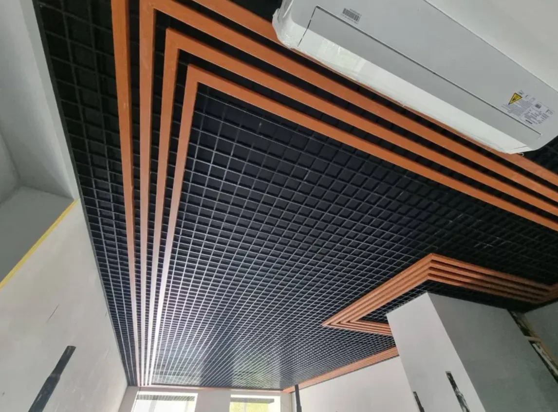Czarny sufit rastrowy z dekoracyjnymi, brązowymi listwami w układzie geometrycznym, widoczny klimatyzator.
