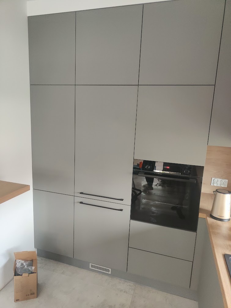 Nowoczesna, szara zabudowa kuchenna z piekarnikiem i szafkami, widoczny karton na podłodze sugerujący montaż.