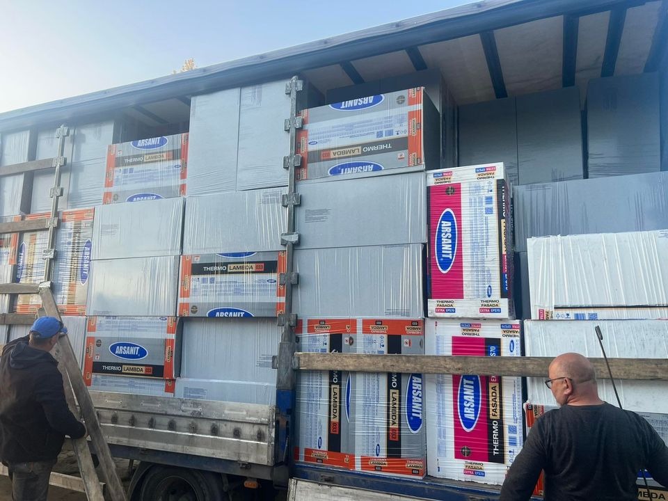 Załadunek materiałów izolacyjnych marki Arsanit Thermo Fasada Lambda na samochód ciężarowy, widoczni dwaj mężczyźni przy pracy, jeden wchodzi po drabinie, drugi nadzoruje załadunek.