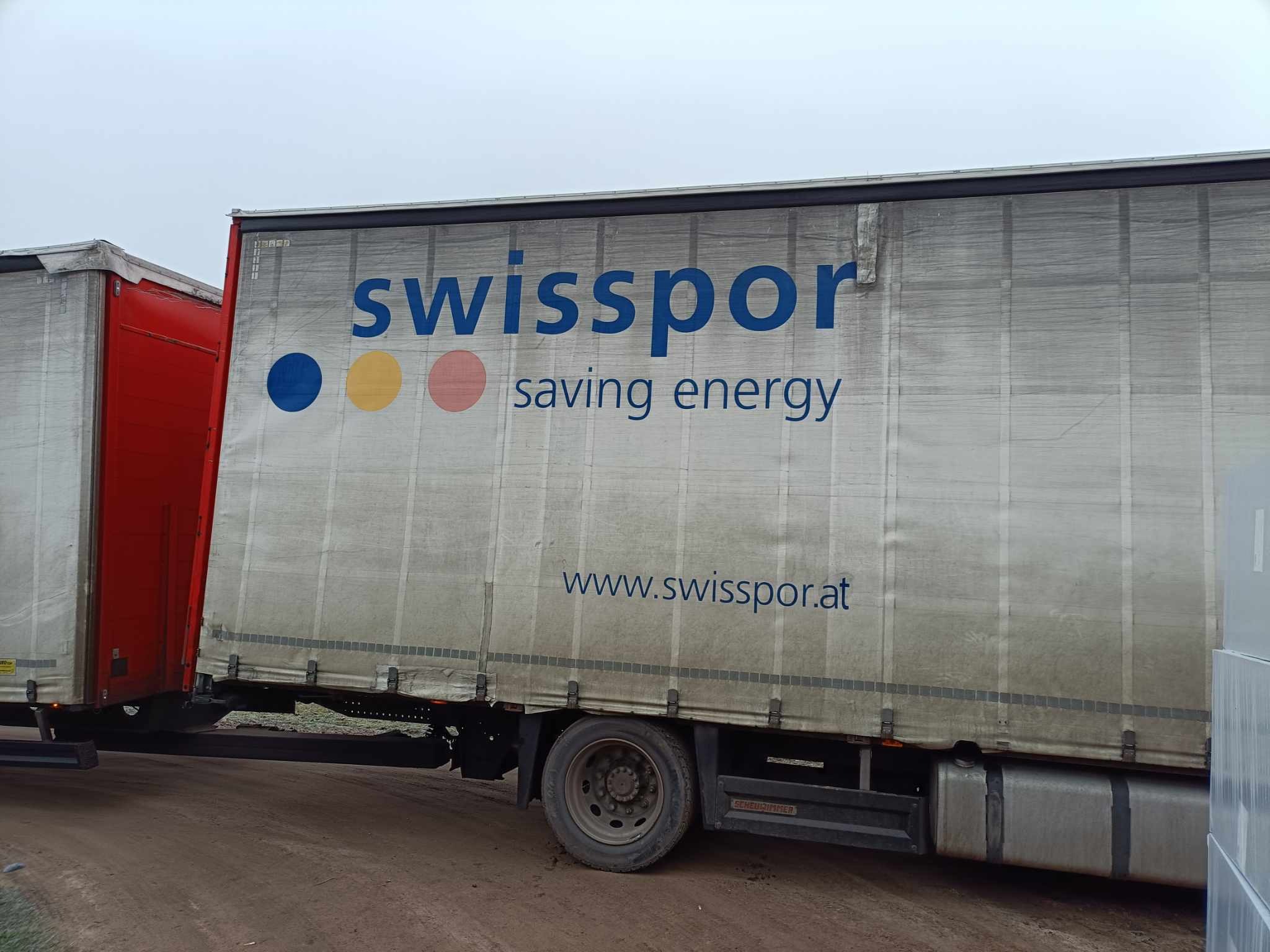 Ciężarówka z naczepą marki Swissopor z nadrukowanym logo i hasłem 'saving energy' na tle pochmurnego nieba.
