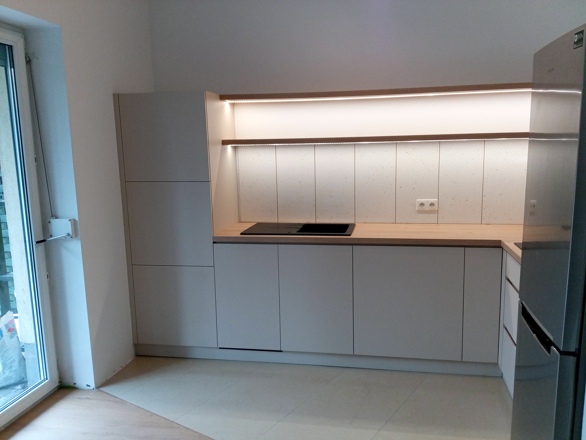 Nowoczesna, minimalistyczna kuchnia z szarymi frontami szafek, drewnianym blatem i oświetleniem LED pod górnymi szafkami, widok z niskiego kąta.