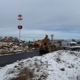 Prace ziemne w zimowej scenerii: koparka Case i spycharka w tle, czarna folia na wykopie. W tle stacja Orlen i KFC.