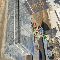 B.U. REM-BUD BOGUSŁAW BUCZKO - Czyszczenie jasnoszarego nagrobka z granitu o wyraźnym wzorze, widoczne kwiaty i znicze na sąsiednich grobach, osoba w trakcie pracy z wiadrem i szczotką.