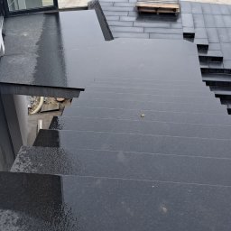 B.U. REM-BUD BOGUSŁAW BUCZKO - Zewnętrzne schody z ciemnego kamienia prowadzące z tarasu w Zapałowie, widok z góry na mokrą powierzchnię stopni i płyt tarasowych.