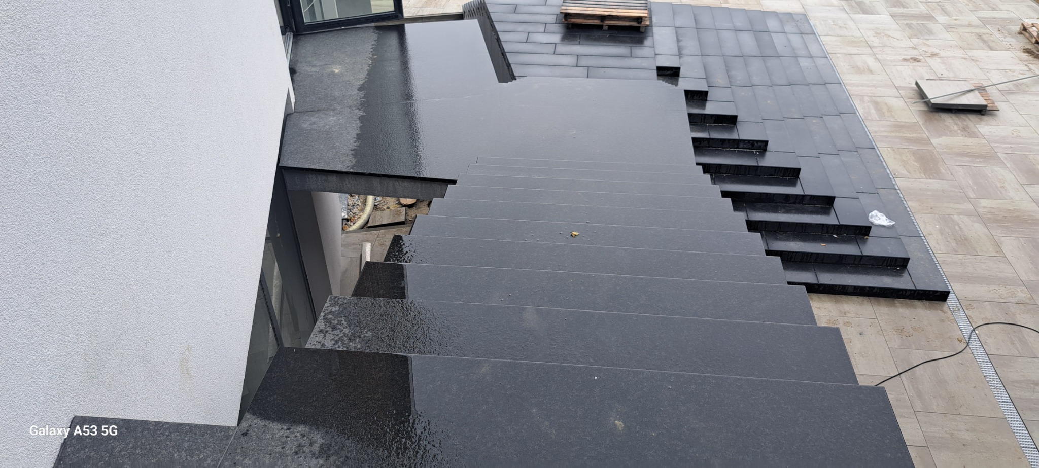 Zewnętrzne schody z ciemnego kamienia prowadzące z tarasu w Zapałowie, widok z góry na mokrą powierzchnię stopni i płyt tarasowych.