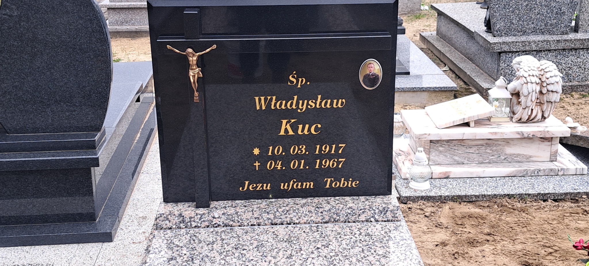 Czarny, granitowy nagrobek z wygrawerowanym imieniem i nazwiskiem Władysława Kuc, datami urodzenia i śmierci, krucyfiksem oraz portretem zmarłego, obok nagrobek z rzeźbą anioła.