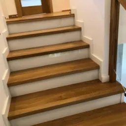 Jasne, dębowe stopnie z białymi podstopnicami i drewnianą balustradą ze szklanym wypełnieniem, widok z dołu.