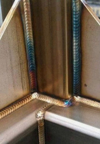 Szczegółowe zbliżenie na precyzyjne spawy łączące metalowe elementy pod kątem prostym, z widocznymi śladami ciepła w postaci tęczowych przebarwień.