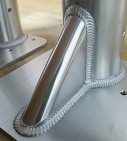 Szczegółowe zbliżenie na precyzyjne spawy łączące rurę ze stalową płytą, widoczne regularne ściegi spawalnicze i gładka powierzchnia metalu.