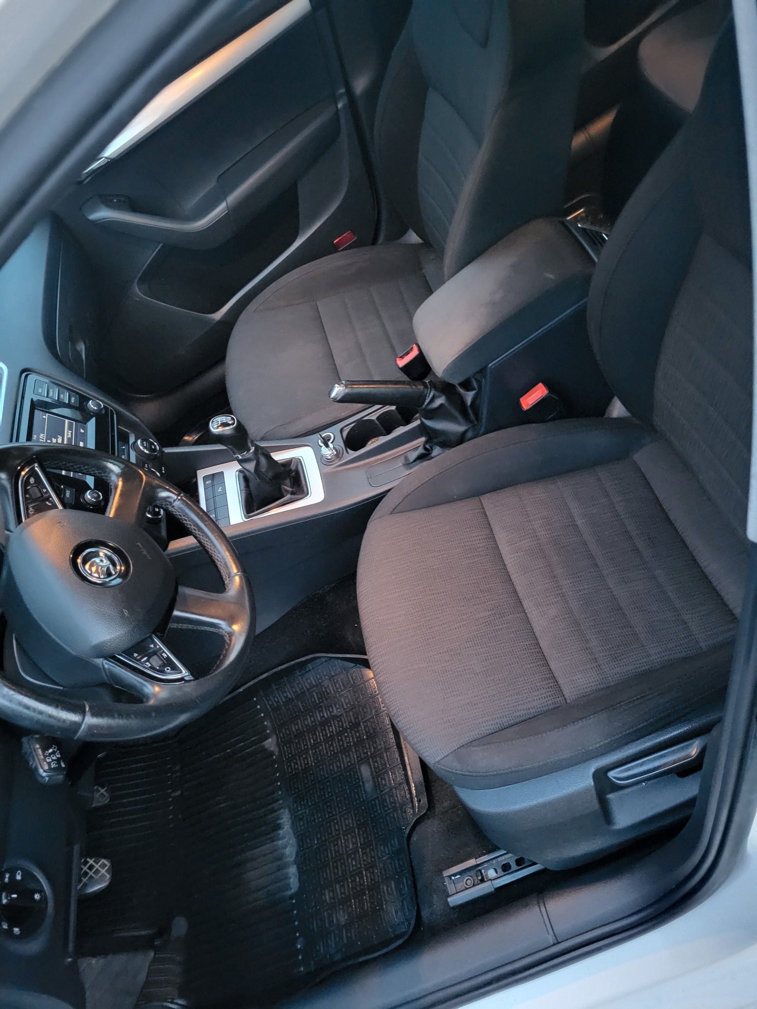 Wnętrze samochodu z widocznymi czarnymi, materiałowymi fotelami, kierownicą z logo, deską rozdzielczą i gumowymi dywanikami.