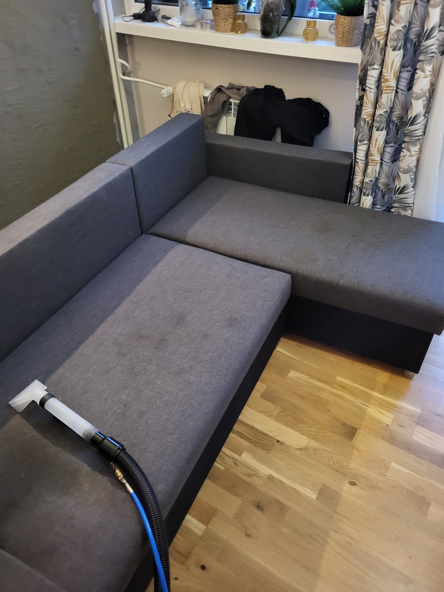 Czyszczenie narożnika tapicerowanym odkurzaczem z niebieskim wężem na drewnianej podłodze.