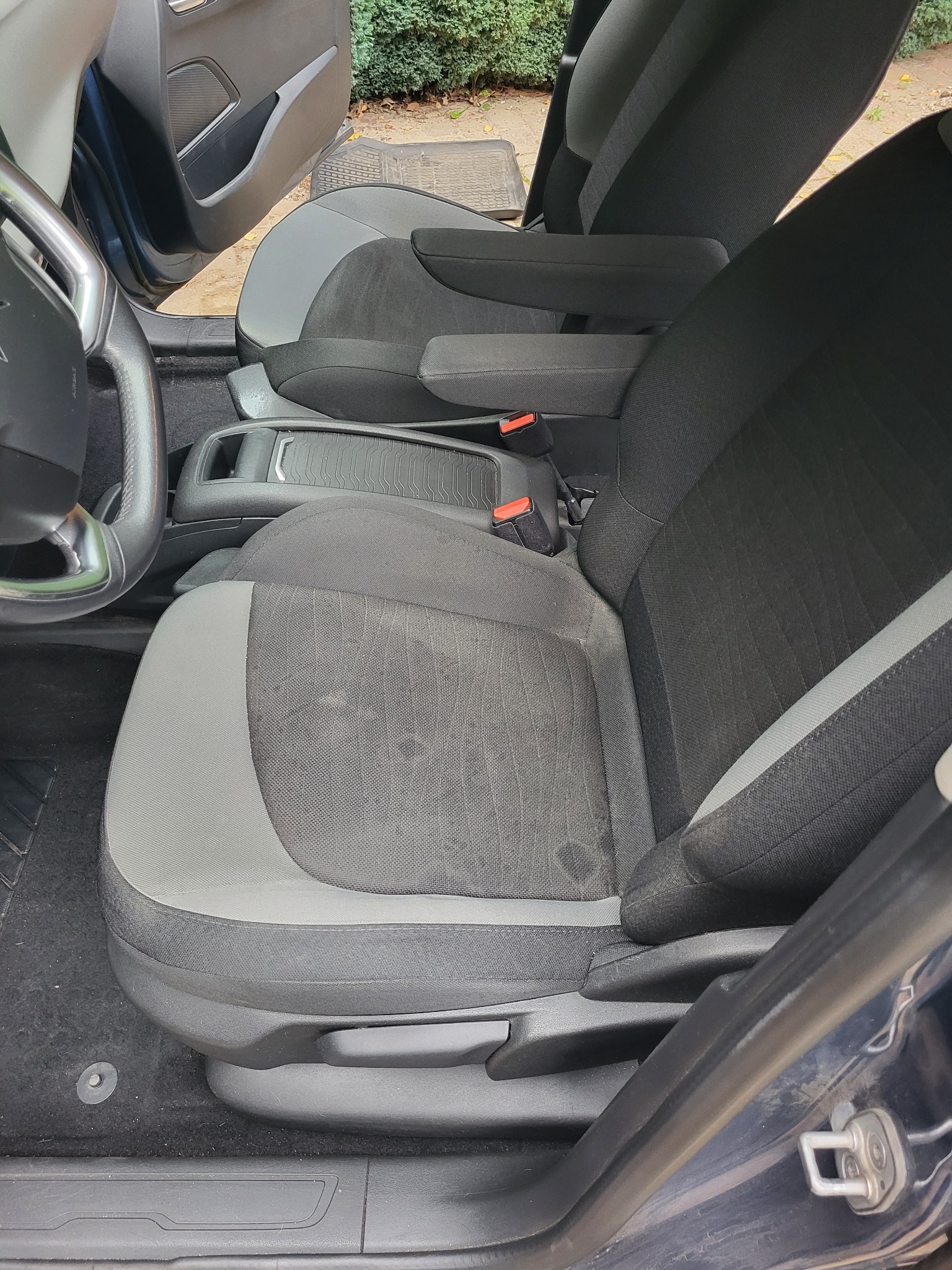 Wnętrze samochodu z widocznymi fotelami z szaro-czarną tapicerką, śladami użytkowania na siedzisku kierowcy i widoczną kierownicą