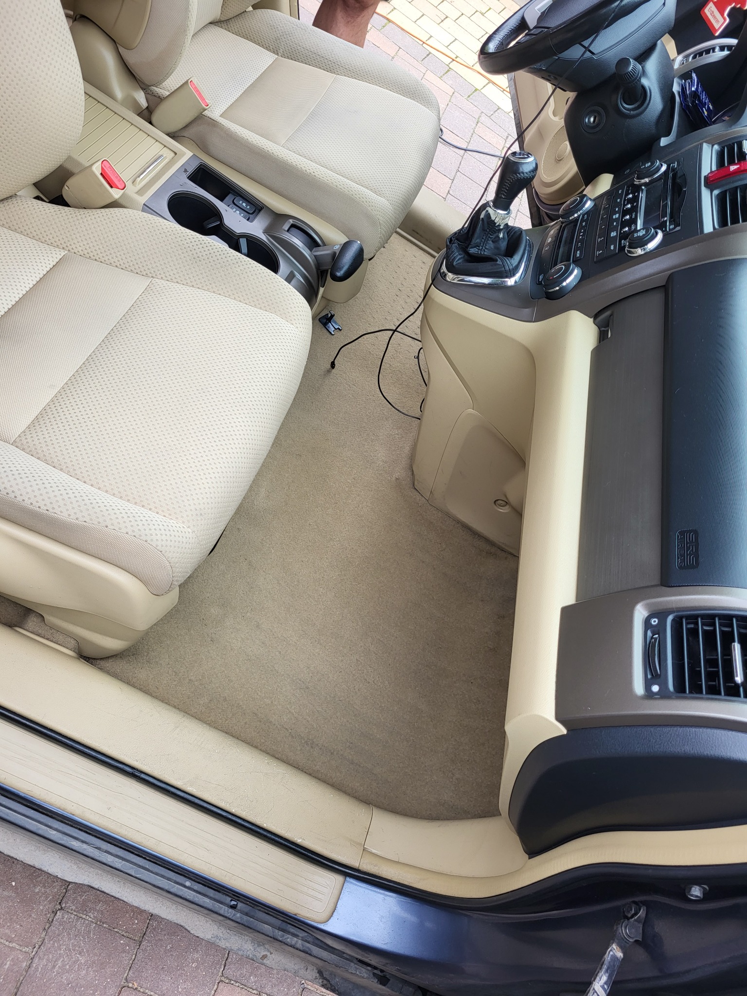 Wnętrze samochodu z beżową tapicerką po czyszczeniu, widoczne fotele, dywaniki i konsola środkowa, z detalami takimi jak dźwignia zmiany biegów i panel klimatyzacji.