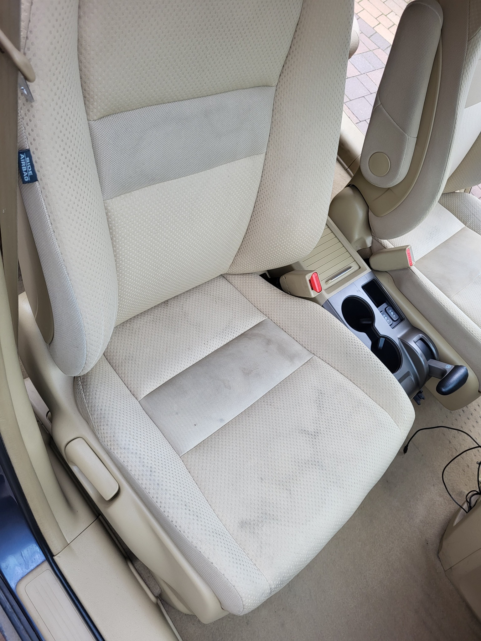 Beżowa tapicerka fotela samochodowego z widocznymi plamami i zabrudzeniami, z boku widoczna etykieta 'Side Airbag'.