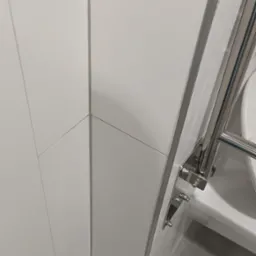 Detal wykończenia łazienki: białe, ukośne płytki ścienne z metalowymi listwami, fragment grzejnika drabinkowego i zawór wody przy podłodze.