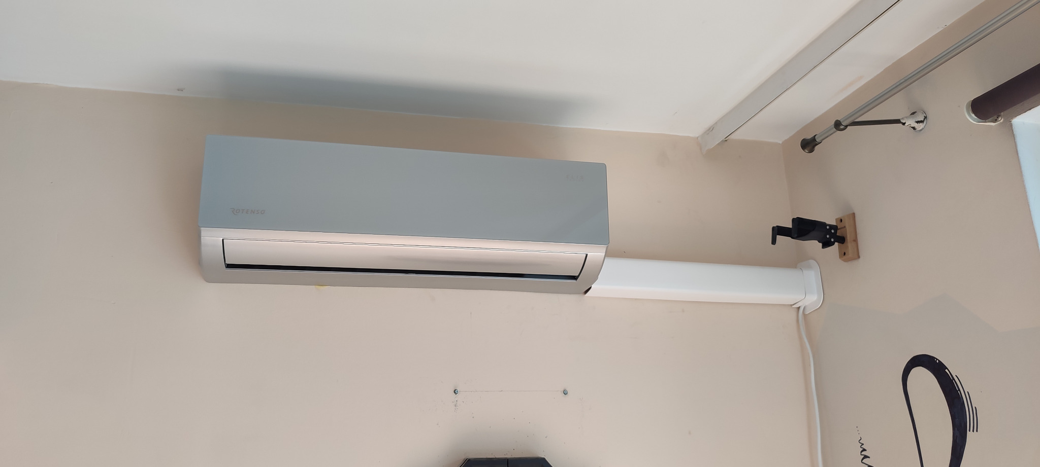 Zamontowany klimatyzator Rotenso w jasnym pomieszczeniu, widoczne rury instalacyjne i uchwyt na ścianie.