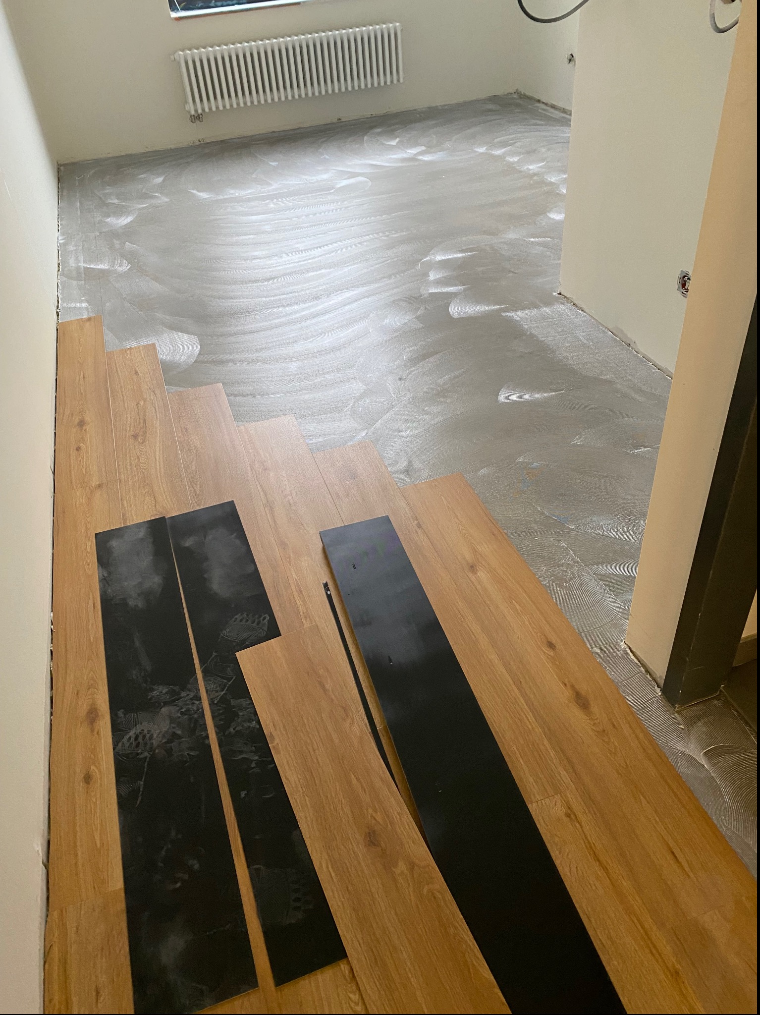 Przygotowanie do ułożenia paneli podłogowych: widoczny podkład klejowy na posadzce, ułożone panele oraz czarne elementy wykończeniowe.