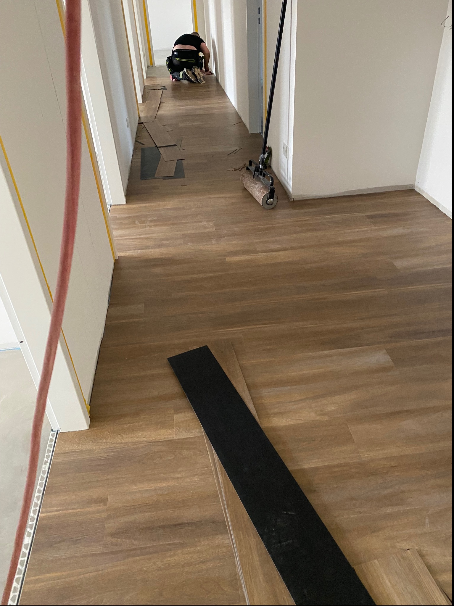 Korytarz w trakcie układania paneli podłogowych, widoczne narzędzia i pracownik w oddali.