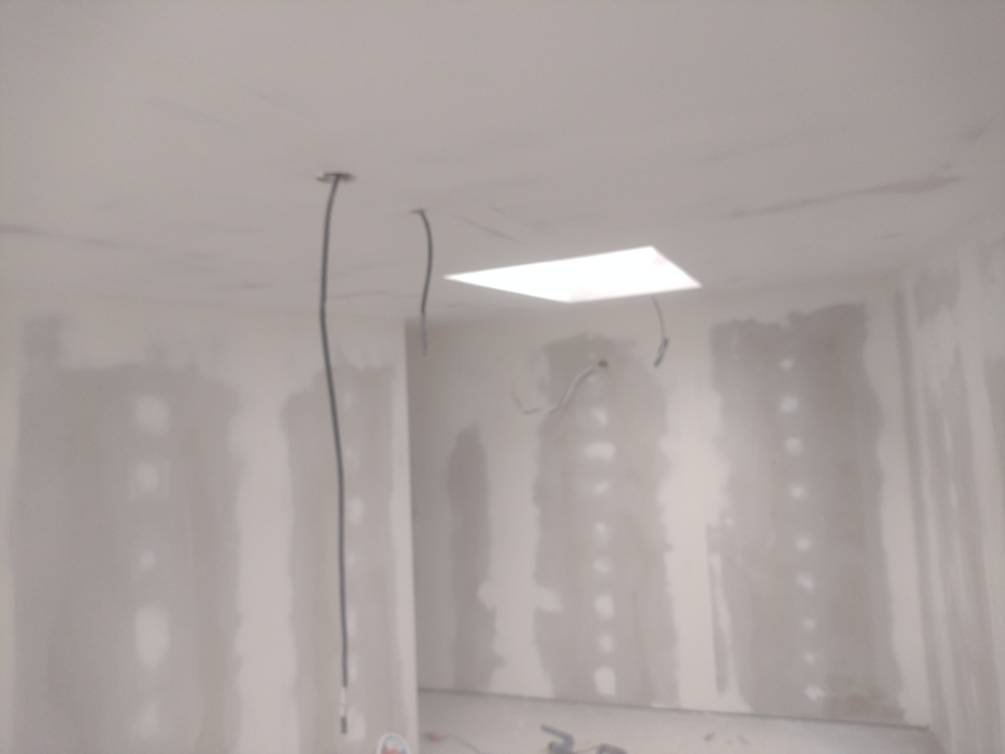 Wnętrze w trakcie prac wykończeniowych: ściany pokryte gładzią, widoczne kable wystające z sufitu, przygotowane pod instalację oświetlenia.