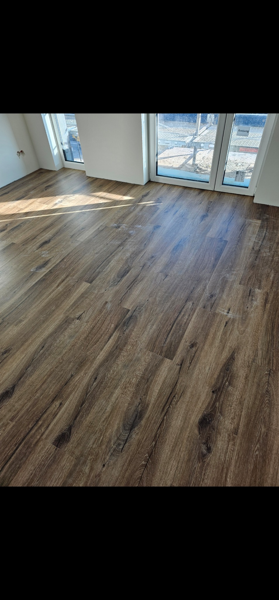 Ukończona podłoga z paneli imitujących ciemne drewno w jasnym pokoju z oknami dachowymi, widoczne promienie słońca.