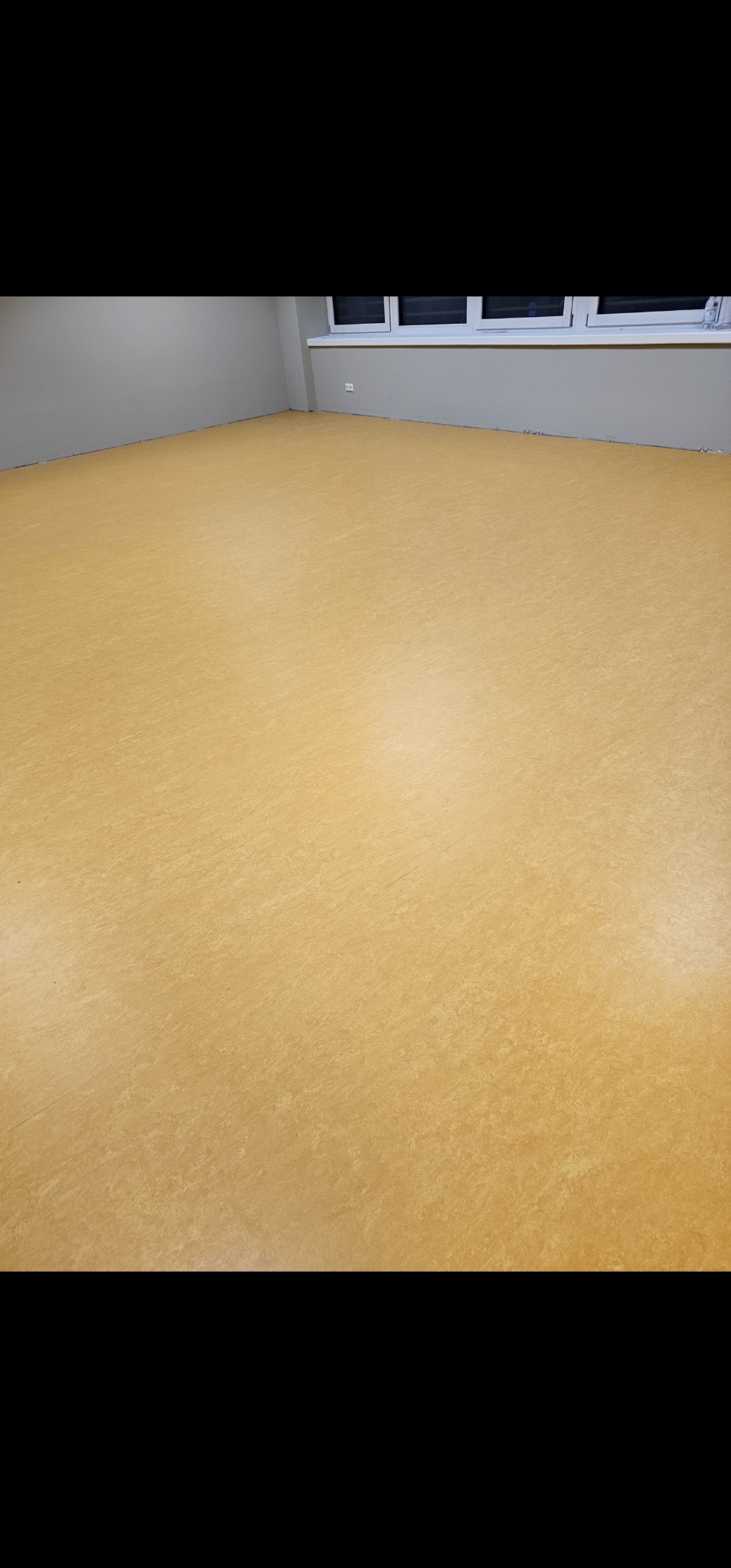 Beżowa podłoga z widoczną strukturą, świeżo ułożona w pustym pomieszczeniu z szarymi ścianami i białym oknem.