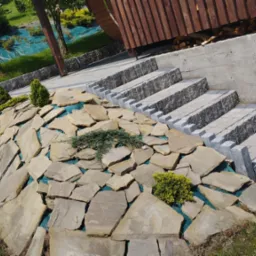 Ułożone nieregularne płyty kamienne na skarpie z roślinami, obok schody z kostki brukowej prowadzące do drewnianej konstrukcji.