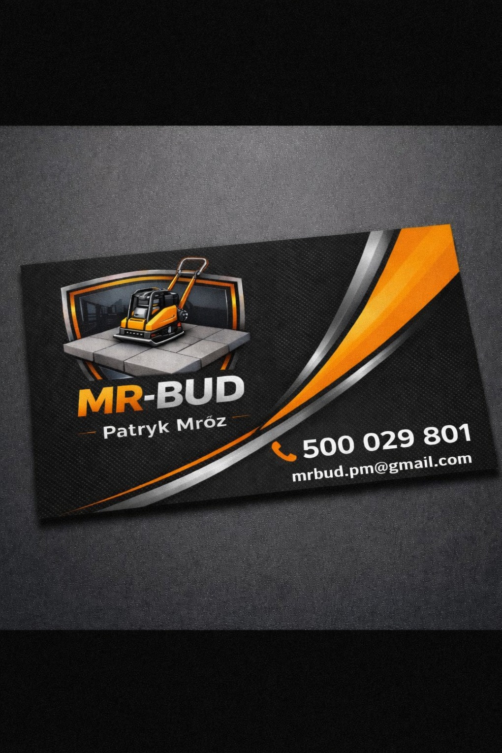 Wizytówka firmy budowlanej z ilustracją zagęszczarki na kostce brukowej, nazwa firmy 'MR-BUD', dane kontaktowe i pomarańczowo-srebrne akcenty graficzne na czarnym tle.