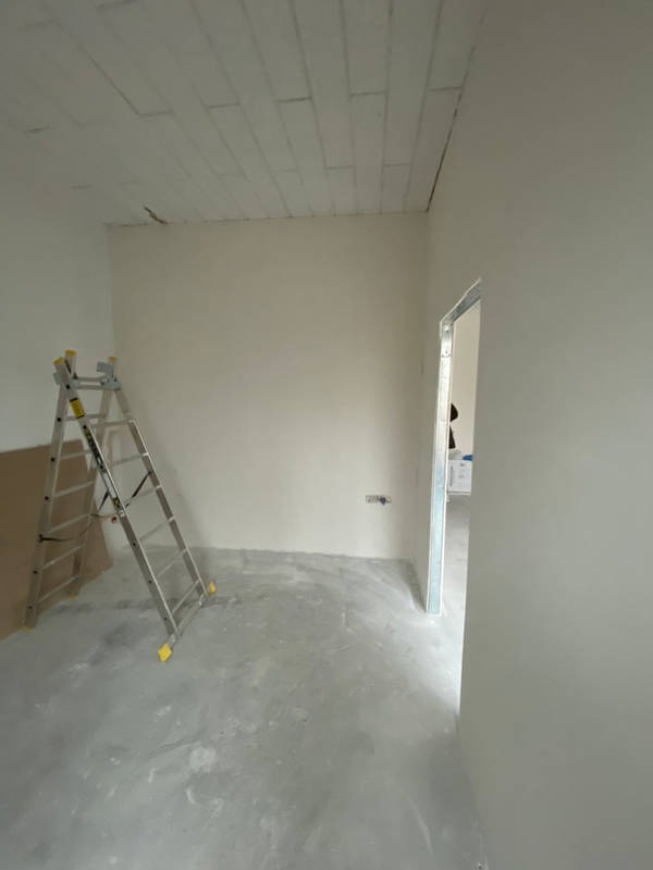 Pokój w trakcie remontu: białe ściany po szpachlowaniu, drabina aluminiowa oparta o ścianę, sufit z widocznymi łączeniami płyt gipsowych, surowa podłoga, widoczne przygotowanie do malowania.