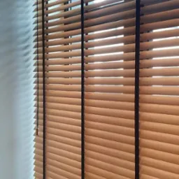 Zamknięte drewniane żaluzje poziome z ciemnymi sznurkami na oknie, widoczne z bliska, z delikatnym światłem wpadającym przez szpary.