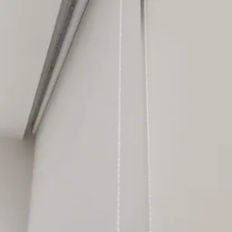 Biała roleta okienna z łańcuszkiem w minimalistycznym wnętrzu w Paczkowie, widok z dołu.