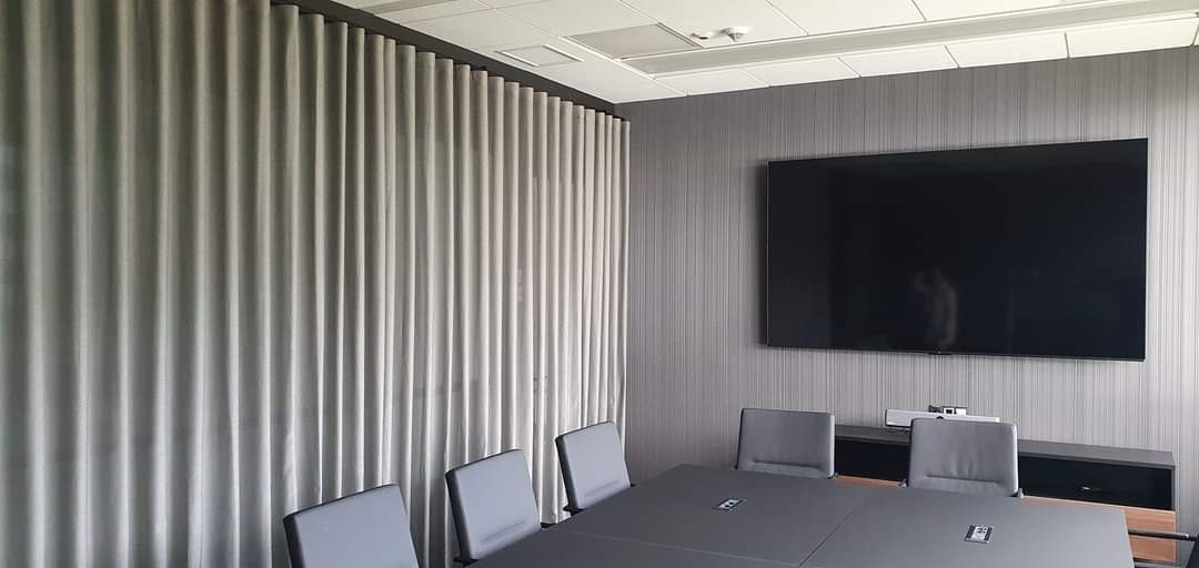 Szare, plisowane zasłony w sali konferencyjnej z szarymi ścianami i dużym telewizorem.