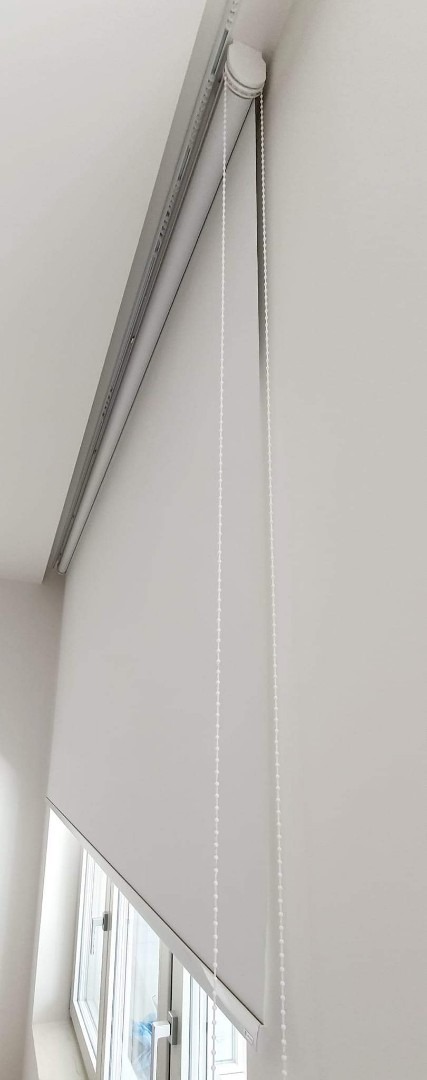 Biała roleta okienna z łańcuszkiem w minimalistycznym wnętrzu w Paczkowie, widok z dołu.