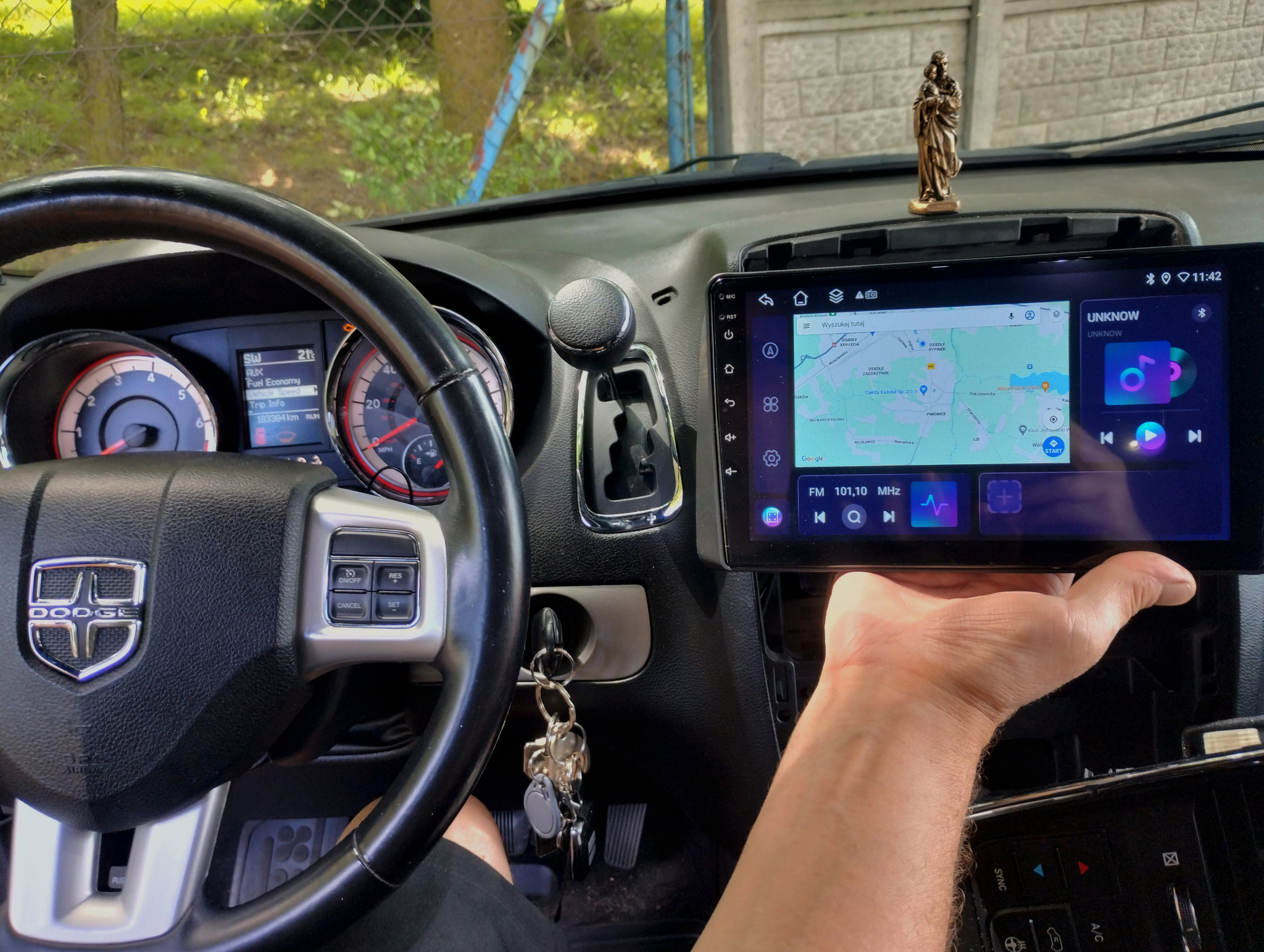 Montaż radia samochodowego z nawigacją GPS w desce rozdzielczej Dodge Durango, widoczny ekran dotykowy z mapą i odtwarzaczem muzyki, statuetka na desce rozdzielczej, kluczyki w stacyjce.