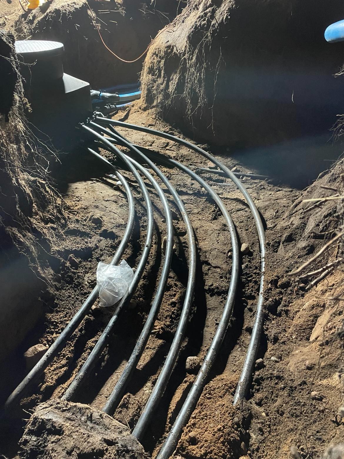 Wykop z ułożonymi rurami instalacji podziemnej, prawdopodobnie związanej z systemem ogrzewania geotermalnego, widoczne złącza i skrzynka przyłączeniowa.