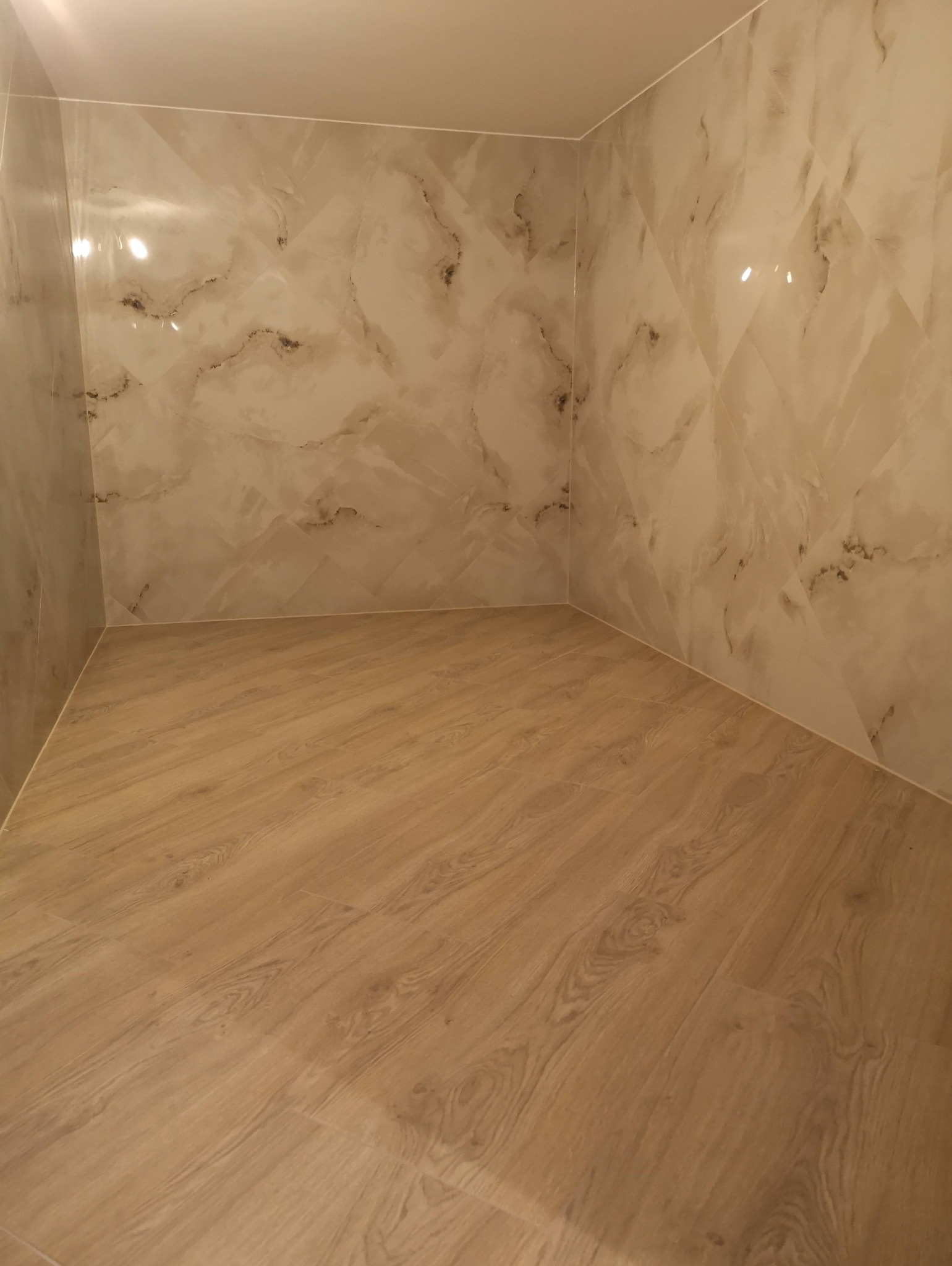 Wykończona łazienka z marmurowymi płytkami ściennymi w odcieniach beżu i brązu oraz podłogą z paneli imitujących drewno w ciepłym odcieniu.