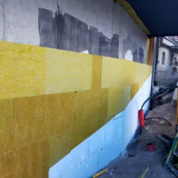 Ocieplanie ściany fundamentowej wełną mineralną na styropianie z widocznymi przewodami instalacyjnymi w wykopie.