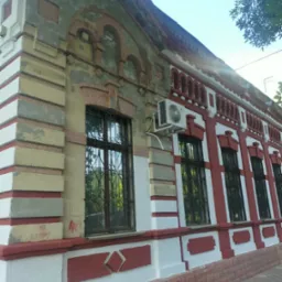 Fragment odnowionej elewacji budynku z czerwono-białymi akcentami, widoczne okna z ozdobnymi kratami, klimatyzator na ścianie i ślady graffiti w dolnej części.