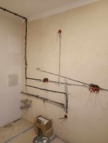 Świeżo położona instalacja elektryczna w surowym pomieszczeniu. Widoczne kable w peszlach przymocowane do ściany, puszki elektryczne w ścianach, brak osprzętu.