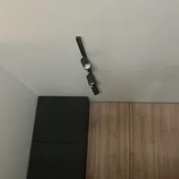 Czarna listwa z trzema reflektorami LED zamontowana na suficie w kuchni, oświetlająca szafki w kolorze drewna i czarne szafki. Minimalistyczny design.