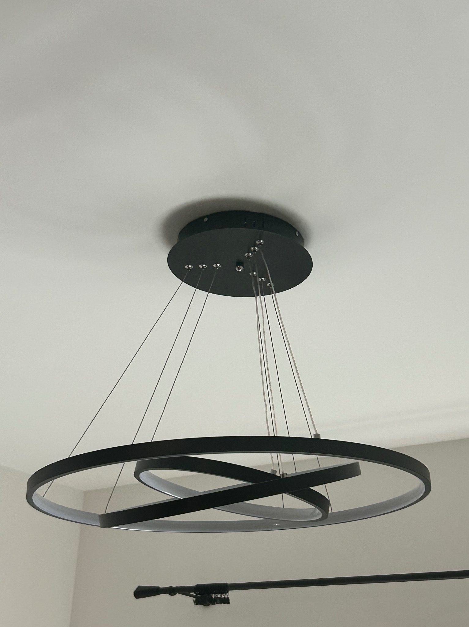 Czarna, nowoczesna lampa wisząca LED z trzema okręgami, zamontowana na suficie. Montaż oświetlenia w Gnieźnie, widok z dołu, oświetlenie wnętrza.