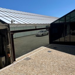 Tedeco - Widok z góry na dziedziniec z kostki brukowej, nowoczesny budynek z przeszkloną fasadą i srebrny samochód w tle, oświetlone jasnym, naturalnym światłem.