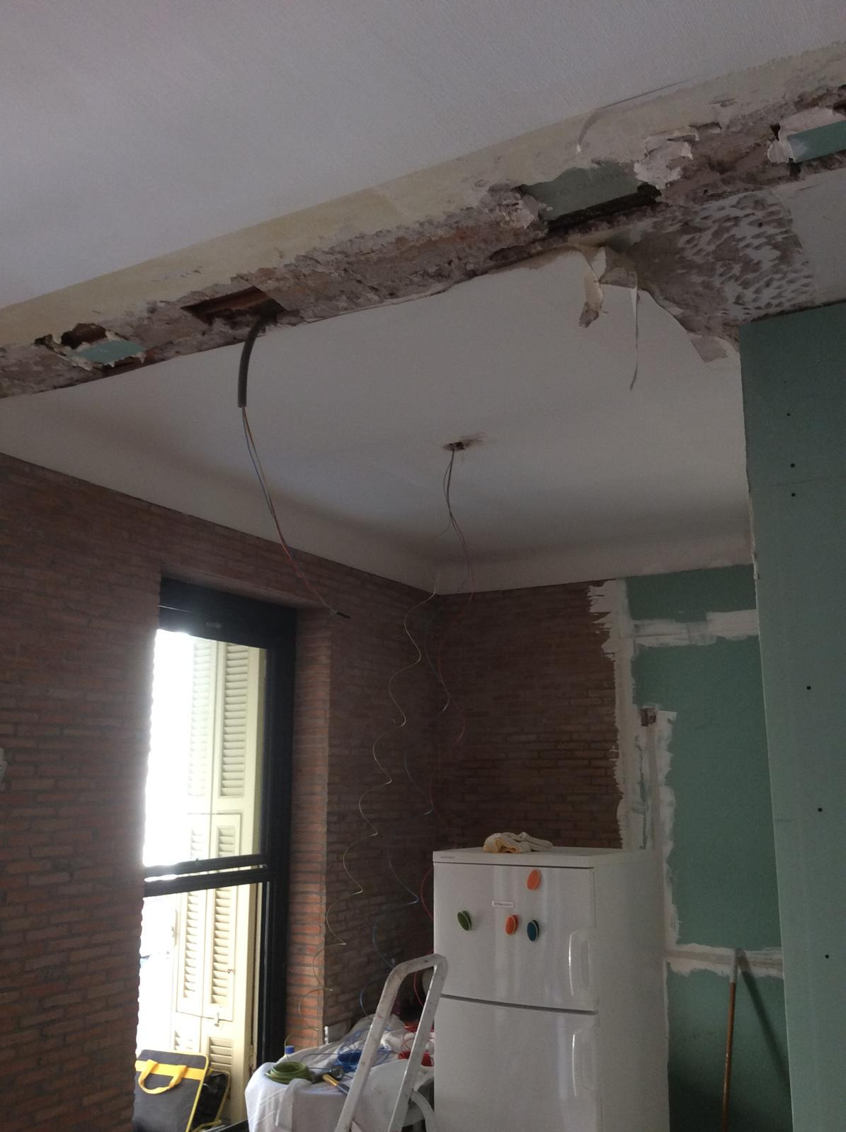 Wrocław: Sufit w trakcie remontu z odsłoniętymi przewodami elektrycznymi, widoczne uszkodzenia i fragmenty starej instalacji, ściany z cegły oraz płyty gipsowo-kartonowe.