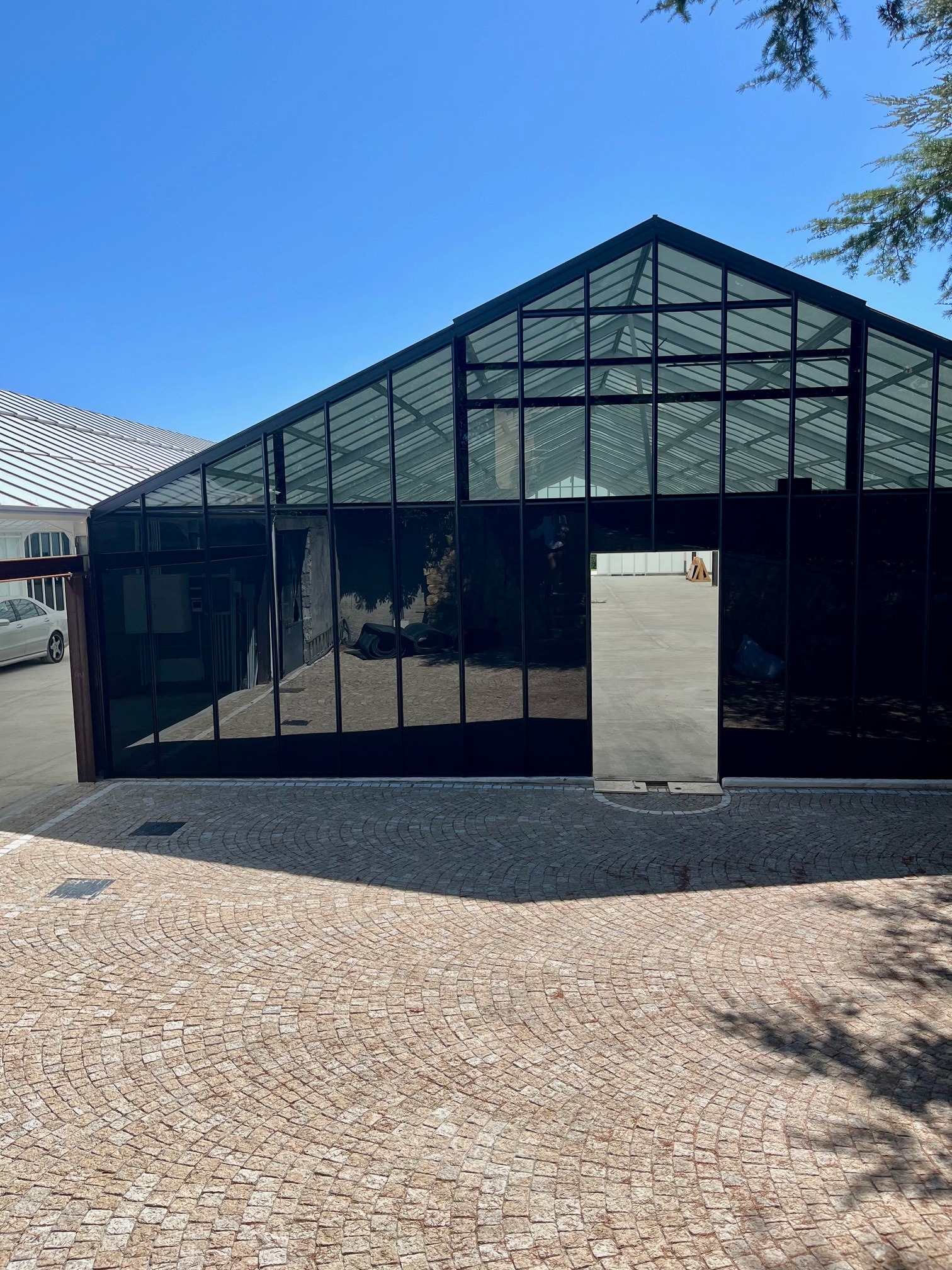 Przeszklona konstrukcja w Wrocławiu, prawdopodobnie szklarnia po modyfikacji, z ciemnymi szybami i metalową ramą, widok z zewnątrz na brukowany plac.