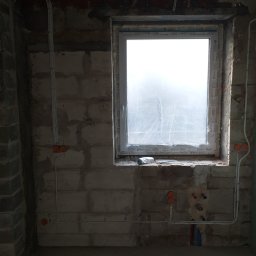 Przemysław Jóźwiak - Surowy stan wnętrza w trakcie prac remontowych: widoczne przewody elektryczne w peszlach, puszki instalacyjne na ścianach z betonu komórkowego oraz okno zabezpieczone folią malarską.