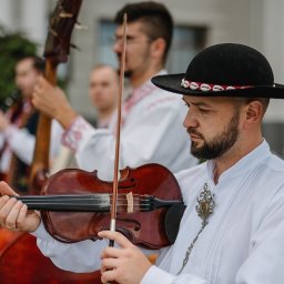 Summer Band - Zespół muzyczny w strojach ludowych, skrzypek w kapeluszu gra na skrzypcach. W tle kontrabasista i klarnecista. Ujęcie z bliska, skupione na skrzypku.