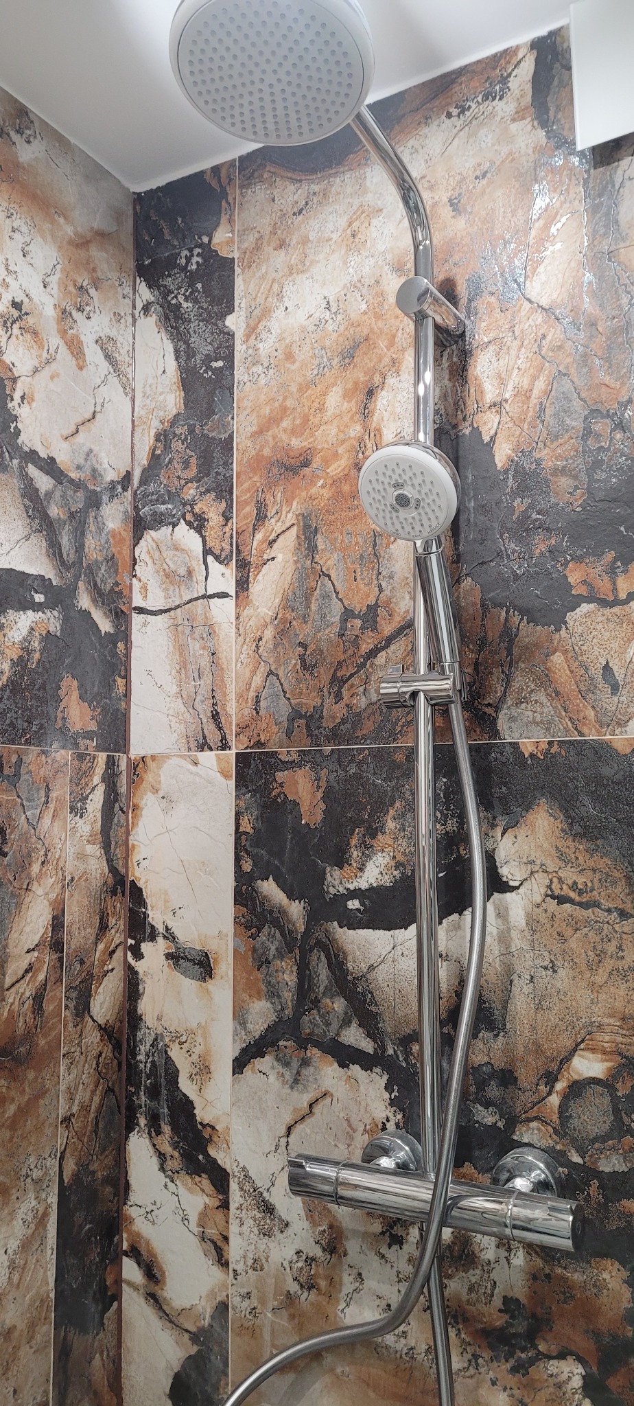 Nowoczesna kabina prysznicowa z dwoma deszczownicami i baterią termostatyczną, wyłożona płytkami imitującymi marmur w odcieniach brązu, beżu i szarości.