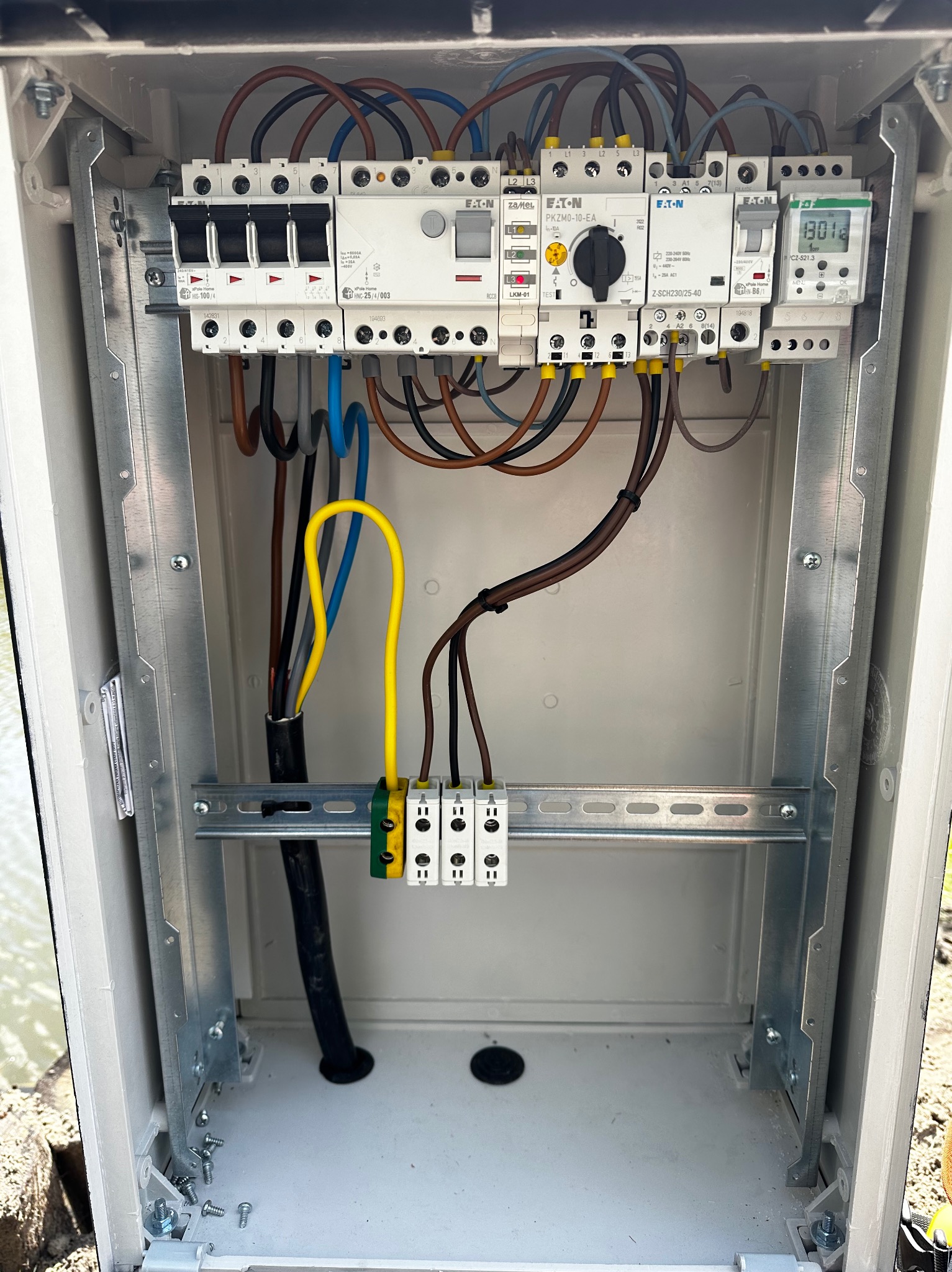 Wnętrze skrzynki elektrycznej z zamontowanymi bezpiecznikami, wyłącznikami różnicowoprądowymi i przewodami o różnych kolorach, zamocowanymi na szynie DIN.